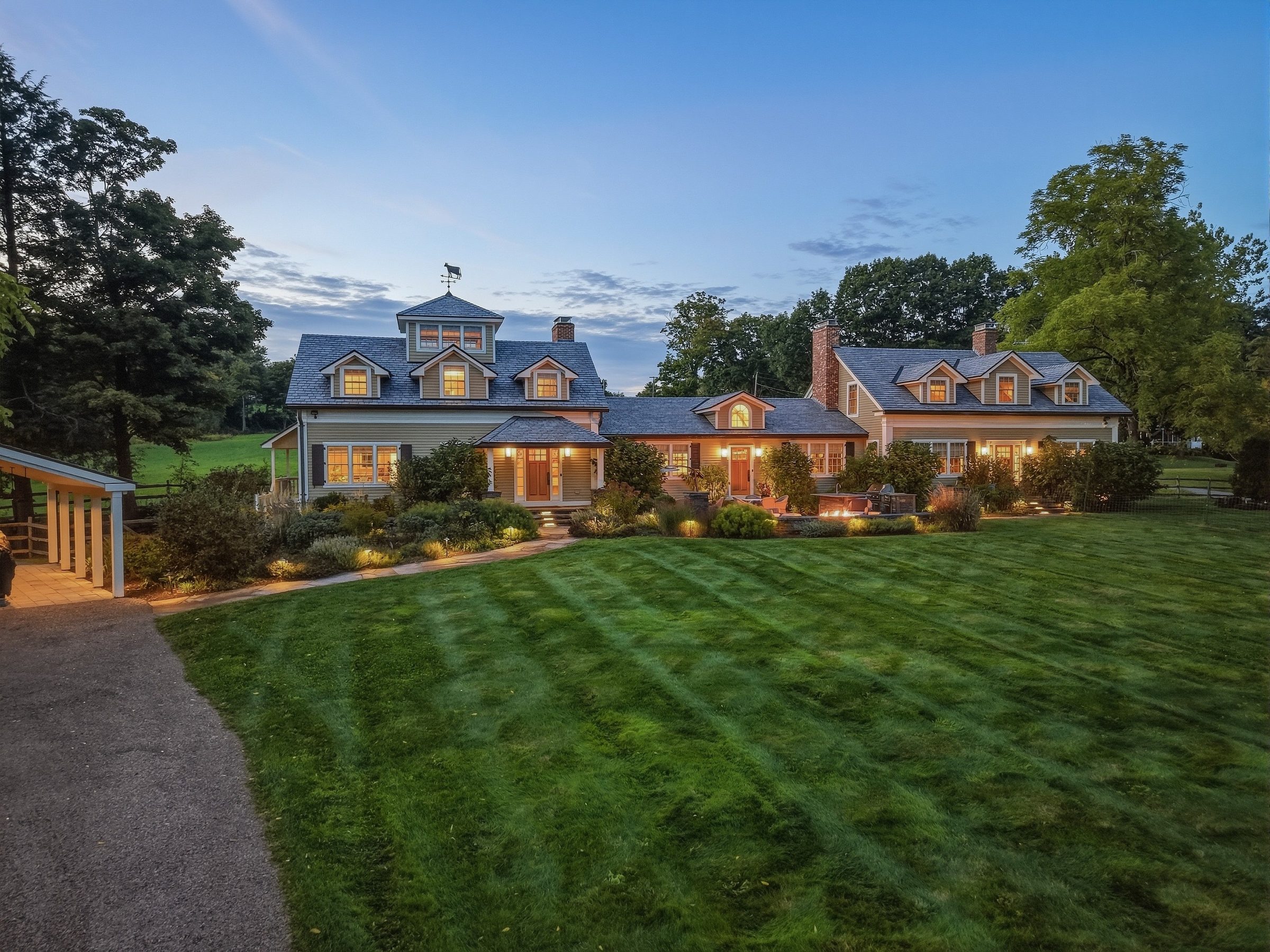 The residence at 54 Patten Road at twilight, its windows lit, with the lawn and meadows beyond