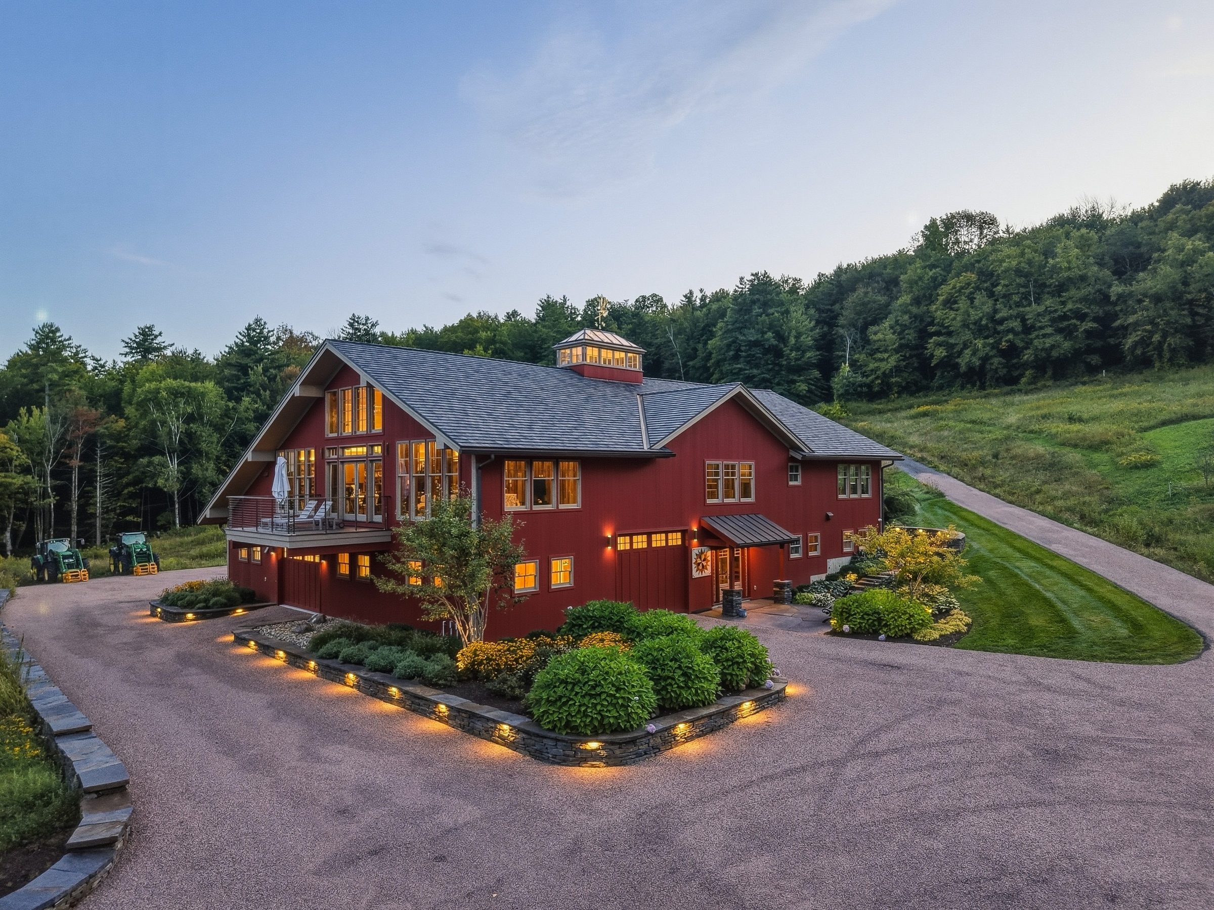 The red converted barn at twilight, its windows glowing above the illuminated drive